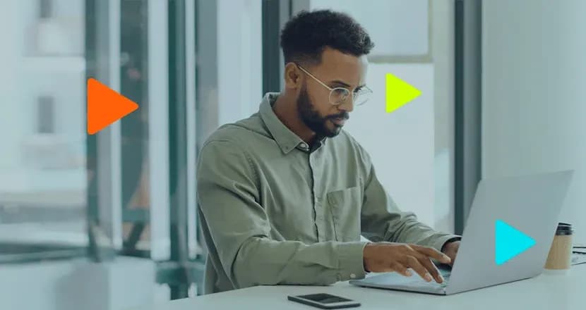 Jovem desenvolvedor negro concentrado trabalhando no notebook em escritório moderno com ícones de play coloridos.